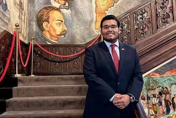 A a smiling Archer Fellow stands in front of a famous staircase with murals