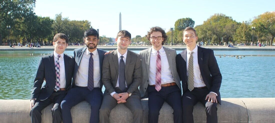 A group of young men sit on the edge of the Reflection Pool with the Washington Monument in the background