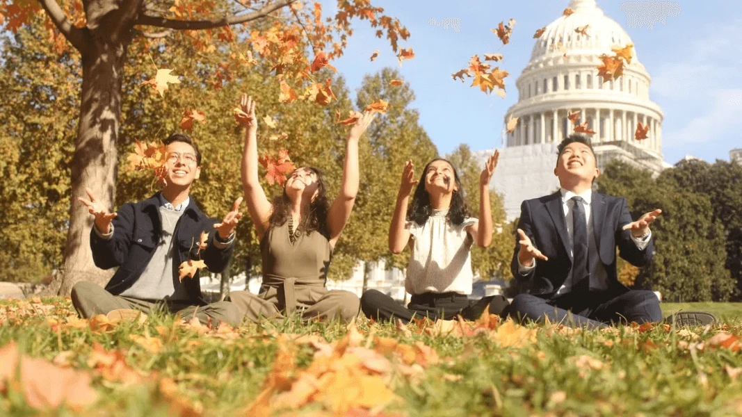 A group of Archer Fellows sit in the grass with fall leaves and the Capitol Building dome in the background.
