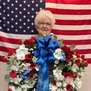 Jean Peterson stands in front of an American flag holding a wreath
