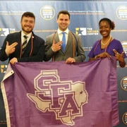 SFA students hold an SFA Flag. Pictured left to right: Nathan Lyons, Casper Dirkx, and Jada Cartwright.