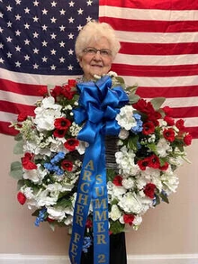 Jean Peterson stands in front of an American flag holding a wreath